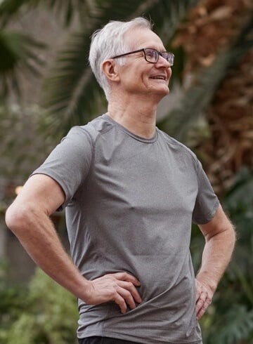 Man with glasses and grey hair putting hands on his hips and smiling to the side