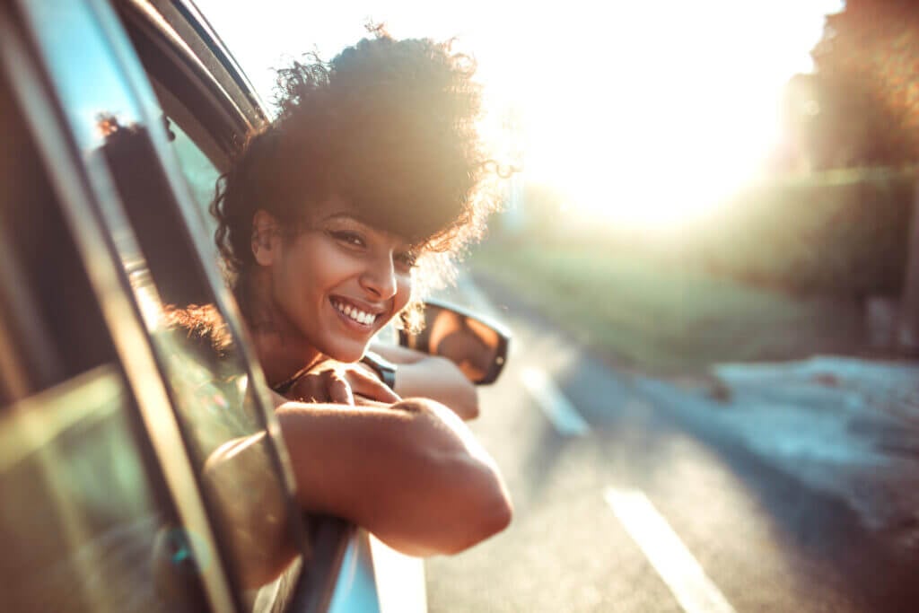 Woman with curly hair leaning out of car window and smiling