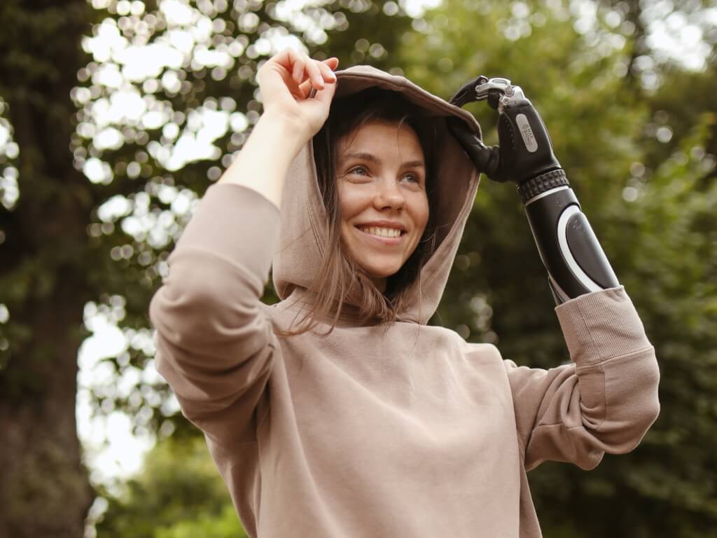 Woman with prosthetic arm pulling her hood back outside
